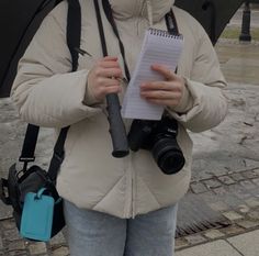 a woman holding an umbrella and looking at a piece of paper with a camera attached to it