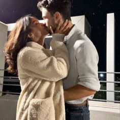 a man and woman kissing each other in front of a building with the lights on