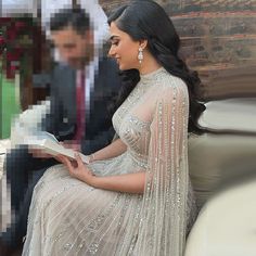 a woman in a white dress sitting on a couch and reading a book with a man standing behind her