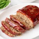 sliced meatloaf on a white plate with green beans