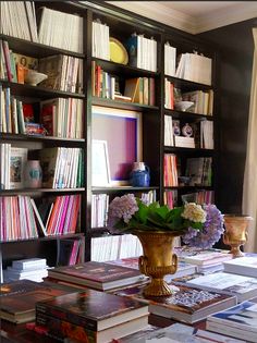 a vase with flowers sitting on top of a table in front of bookshelves