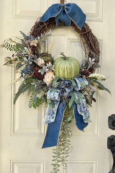 a wreath is hanging on the front door with blue ribbon around it and flowers, greenery, and leaves