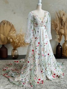 a white dress with red and green flowers on it sitting on a mannequin