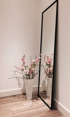 a vase with pink flowers sitting in front of a mirror on the floor next to a wall