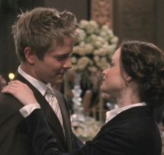 a man and woman standing next to each other in front of a table with flowers