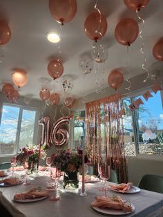 a table set up for a party with balloons and streamers hanging from the ceiling