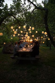 people sitting at a picnic table with paper lanterns hanging from the trees