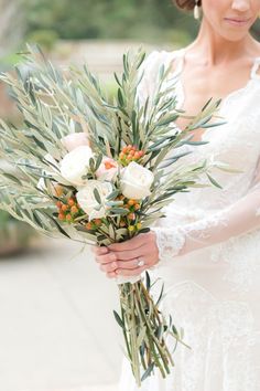 a woman holding a bouquet of flowers and greenery in her hands while wearing a wedding dress