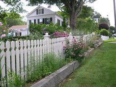 a white picket fence in front of a house with pink flowers growing on the side