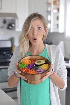 a woman holding a wooden bowl filled with lots of different types of food in it