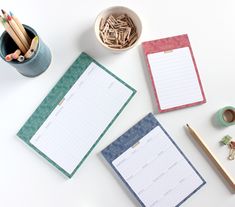 three notebooks and two pencils on a white table with other office supplies next to them