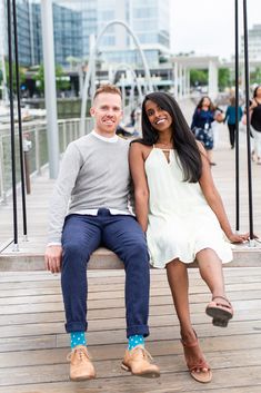 a man and woman sitting on a bench in the middle of a pier with buildings in the background