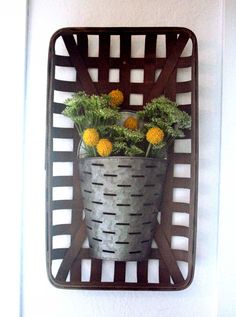 a metal basket filled with yellow flowers on top of a white wall next to a door