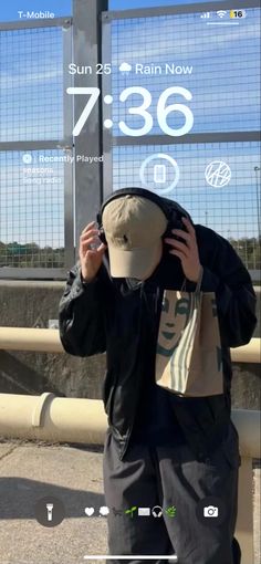 a person standing in front of a fence with a hat on their head looking at the clock