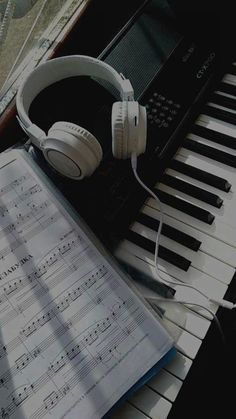 an open book with headphones on top of it next to a keyboard and piano