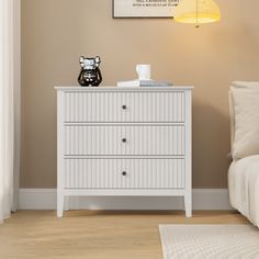 a white dresser sitting next to a bed in a room with a lamp on top of it