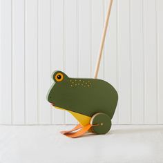 a green frog toy on a white surface with a wooden stick sticking out of it's mouth