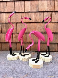 three pink flamingos standing on top of wooden bases