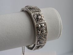 I estimate that this lovely and RARE Topazio Portuguese bracelet was made in the 1960s.  It is embellished with repoussé icons on each of its 12 panels: roses, fruits, corn, garden urn, grapes and ivy.   The catch holds tightly and it sports a safety chain for added security.  The outside of the bracelet is in excellent vintage condition.  It is rare to see a repoussé bracelet without any dents!  I see one small dent ON THE INSIDE at the hinge.  See the last photo for detail.  On the outside, th Vintage Bracelets Silver, Vintage Antique Silver Bangle Bracelet, Corn Garden, Vintage Bangle Bracelet With Box Clasp, Vintage Sterling Silver Hinged Bracelets, Vintage Silver Bracelet With Box Clasp, Vintage Tarnish-resistant Bracelets, Bracelet Aesthetic, Unique Jewelry Vintage