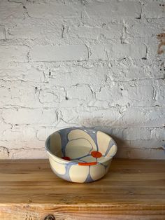 a bowl sitting on top of a wooden table next to a white brick wall,