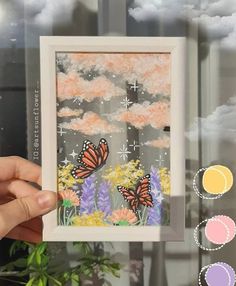 a hand holding up a framed photo with some flowers and clouds in the back ground