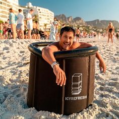 a man is sitting in a large trash can on the beach while people stand around him