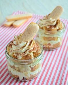 two small glass jars filled with desserts on top of a red and white table cloth