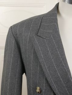 This handsome gray pinstripe double-breasted blazer has peak lapels and padded shoulders, and closes in the front with one faux tortoiseshell button (six in total show on the front). Three buttons also decorate each sleeve edge. The German jacket has three pockets on the front, and is lined in a silvery gray satin viscose fabric. Brand: International Style (Germany) Size: 40 US/UK Material: 70% wool, 30% polyester Condition: Excellent (clean, soft, and supple, with no stains, tears, wear spots, Double-breasted Pinstripe Blazer For Tailoring, Pinstripe Double-breasted Tailoring Blazer, Pinstripe Lapel Collar Outerwear For Formal Occasions, Formal Pinstripe Outerwear With Lapel Collar, Classic Double-breasted Pinstripe Outerwear, Classic Pinstripe Outerwear With Lapel Collar, Double-breasted Pinstripe Blazer For Formal Occasions, Classic Striped Double Breasted Suit For Office, Classic Pinstripe Blazer With Lapel Collar