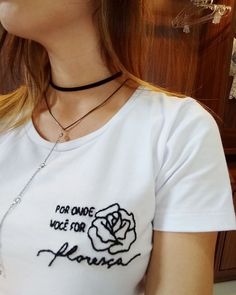 a woman wearing a white t - shirt with a rose on the chest and a black choker around her neck