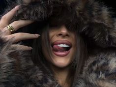 a woman wearing a fur coat and holding her hands up to her face with one hand