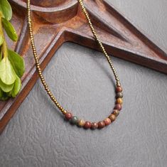 This is a dainty beaded necklace in a combination of earthy red creek jasper stones and tiny bronze seed beads. The stones include shades of red, green, ochre and tan - each stone is unique. The necklace is finished with an antiqued brass plated hook and eye clasp. You can add an optional brass plated 2-inch extender chain for added versatility or peace of mind if this is a gift. This earthy necklace is casual enough for everyday wear. It is lightweight and the optional extender chain would make it easy to layer with some other faves. Necklace length: approx. 16"; optional 2" extender chain available Beaded Necklace Collection: https://www.etsy.com/shop/BonArtsStudio?ref=seller-platform-mcnav&section_id=17053954 See What's New: https://www.etsy.com/shop/BonArtsStudio?ref=seller-platform-mc Earthy Polished Beads Jewelry As Gift, Earthy Tiny Beads Jewelry As Gift, Bronze Necklace With Polished Beads As Gift, Earthy Tiny Beads Jewelry For Gifts, Earthy Tiny Beads Jewelry Gift, Hand-strung Jasper Necklaces As A Gift, Hand-strung Jasper Necklaces For Gifts, Earthy Beaded Necklaces With Polished Beads For Gifts, Earthy Round Beads Necklace For Gift