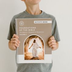 a young boy holding up a book about the bible