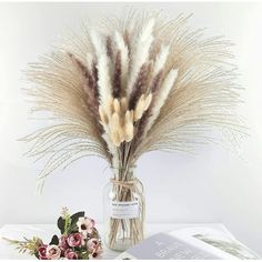 dried flowers in a glass vase next to an open book on a white tablecloth