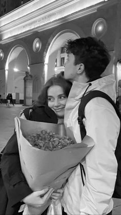 a man holding a bouquet of flowers next to a woman in a white shirt and black backpack