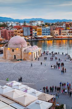 many people are walking around in front of the water and buildings with umbrellas on them