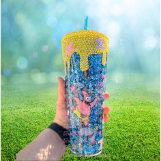 a person holding up a plastic cup filled with blue and yellow beads on top of green grass