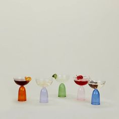 four different colored glasses with fruit in them sitting next to each other on a white surface