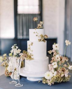 a white wedding cake sitting on top of a table next to wine glasses and flowers