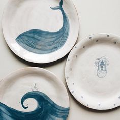 three ceramic plates with designs on them sitting on a white tablecloth covered surface, one has a blue whale and the other is a boat