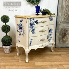 a white dresser with blue flowers painted on it and potted plants next to it