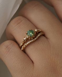 a woman's hand with a green ring on top of her finger and diamond band