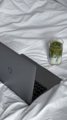 an apple laptop computer sitting on top of a bed next to a glass of liquid