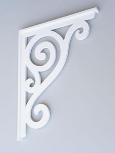 an ornate white shelf bracket on a gray wall with swirly scrolls in the corner