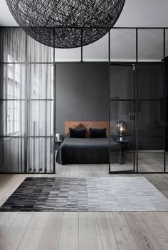 a bedroom with glass walls and a bed in the middle, along with a large black chandelier hanging from the ceiling