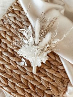 a woven basket with some white flowers and feathers on the top, next to a cloth