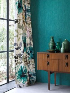 a teal room with green walls and vases on a dresser next to the window