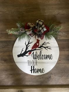 a welcome sign on a wooden wall with pine branches and plaid bow hanging from it