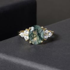 Elevate your love with our Oval Classic Moss Agate Cluster Engagement Ring. This timeless piece boasts a stunning oval-shaped moss agate stone, surrounded by a cluster of smaller gems. The unique combination of colors and textures creates a truly one-of-a-kind ring that will be cherished for years to come. Make a statement and capture the beauty of nature in every moment. Main Stone: Moss Agate, 8x10mm  Side Stones: Colourless Zircon Accents VS to VVS clarity Band: 1.4-1.6mm bandwidth Band Material: 14k Gold, 18k Gold, Platinum Conflict-Free  ** This item is 100% handmade, which requires 3 weeks lead time. Moss Agate Jewelry, Moss Agate Stone, Moss Agate Ring, Cluster Engagement Ring, Agate Jewelry, Agate Ring, Cz Diamond, Beautiful Gift Boxes, Agate Stone