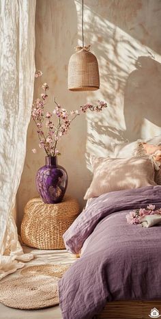 a bed with purple sheets and pillows next to a vase filled with flowers on top of it