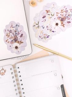 an open planner with flowers on it next to a pen